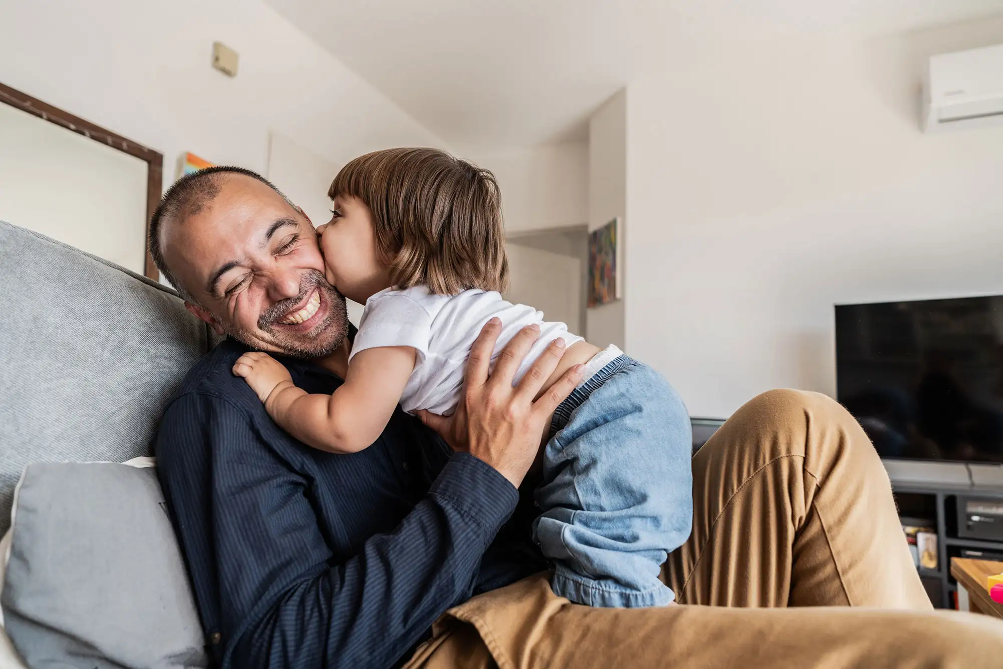 Toddler kissing laughing father on couch at home