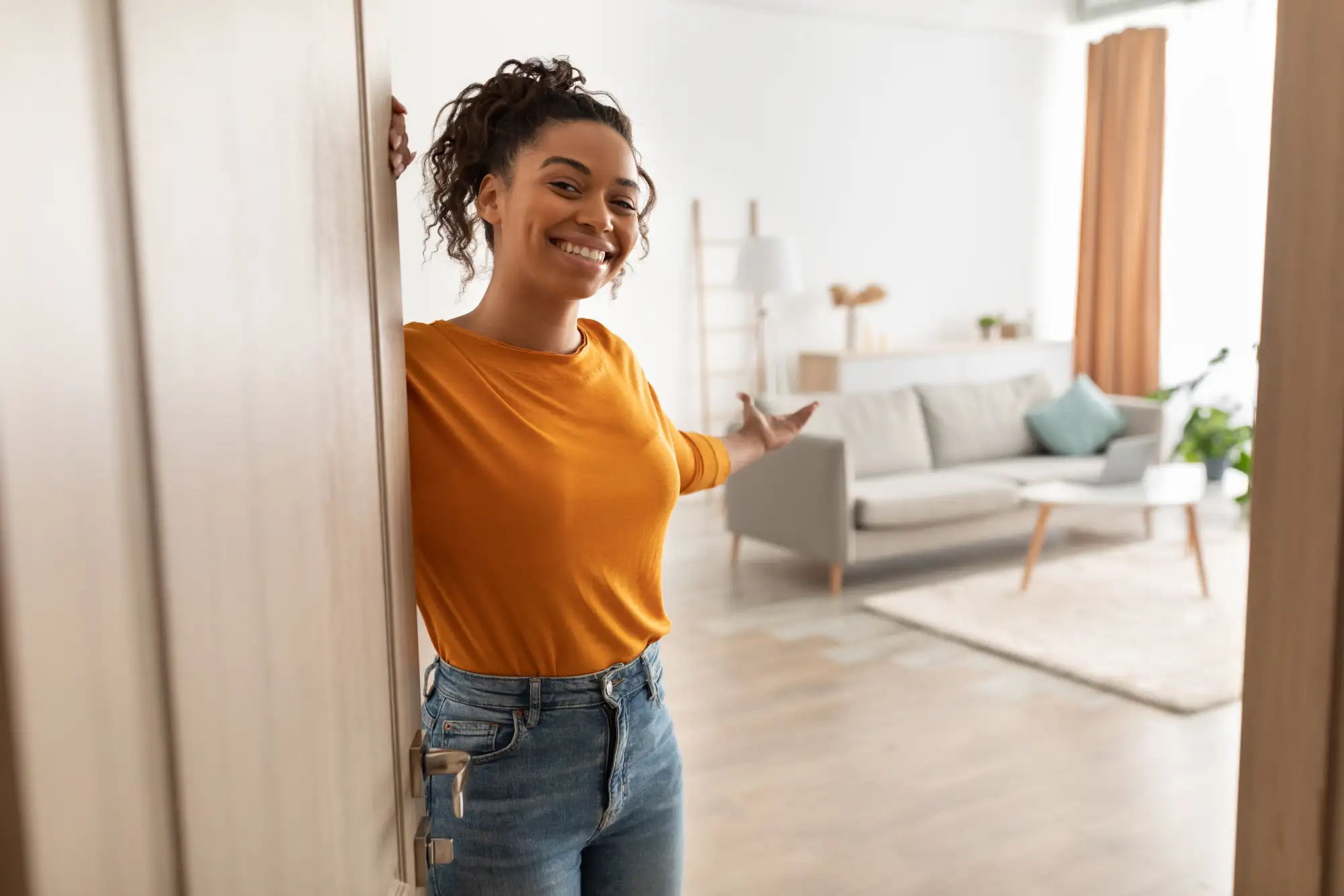 Smiling woman opening door welcoming guests into modern living room